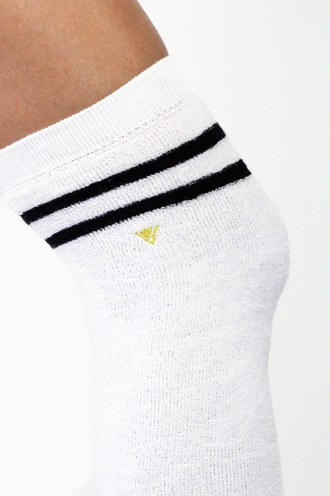 Detail picture of Arebesk gold logo embroidered on the side of white terry legwarmers with black stripes.