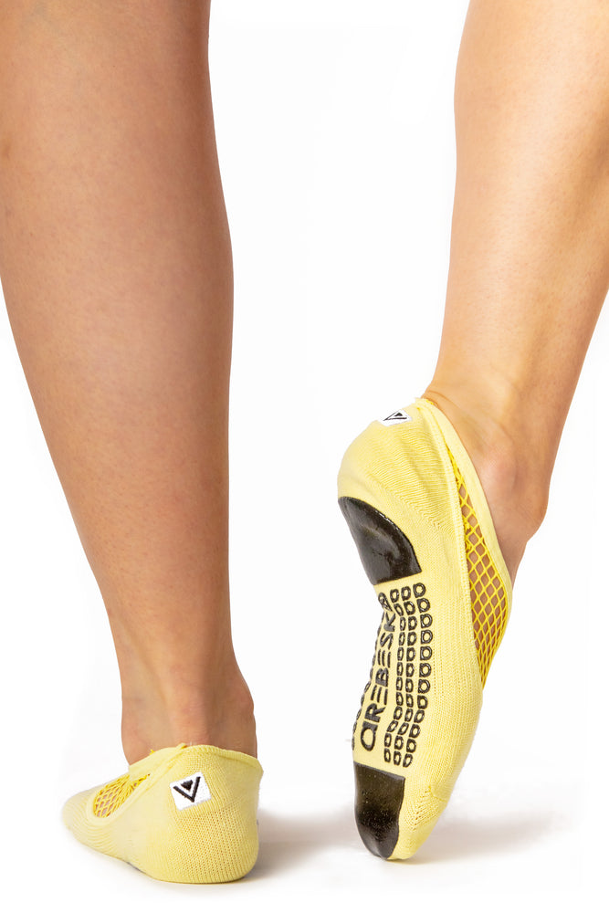 Back view of yellow ankle height, scooped grip socks with a diagonal mesh panel extending from the outside of the ankle to the top of the toes.