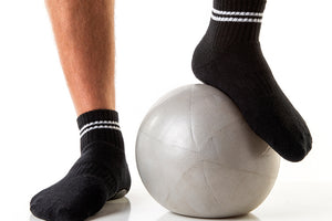 Men's black low crew socks with white stripes and white triangular Arebesk logo, pictured with gray exercise ball.
