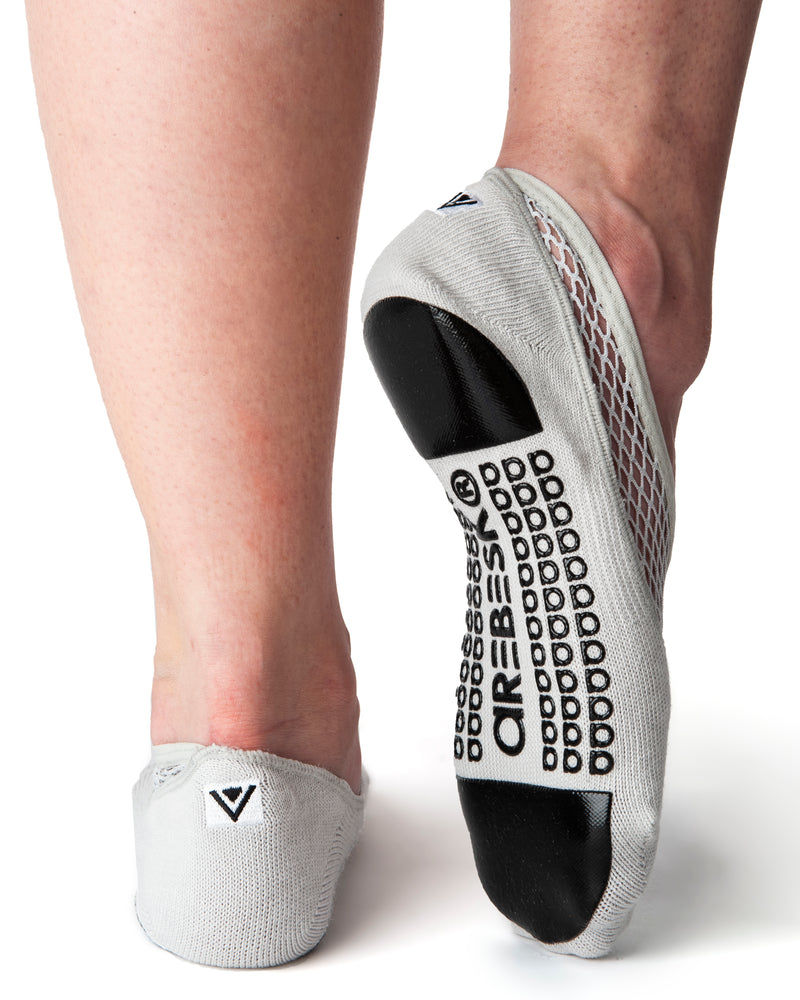 Back view of light gray ankle height, scooped grip socks with a diagonal mesh panel extending from the outside of the ankle to the top of the toes. Grip design has a silicon pad on the ball of the foot and the heel, as well as grip spelling out 'Arebesk" surrounded by rows of additional a's in the center of the foot.