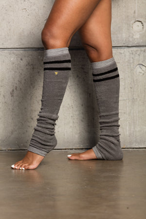 Side view of gray terry legwarmers with black stripes accented with a gold Arebesk embroidered logo.
