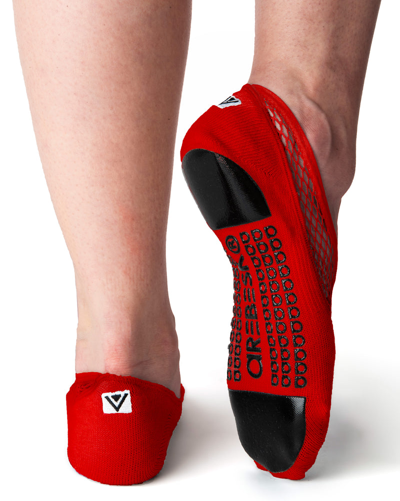 Back view of red ankle height, scooped grip socks with a diagonal mesh panel extending from the outside of the ankle to the top of the toes. Grip design has a silicon pad on the ball of the foot and the heel, as well as grip spelling out 'Arebesk" surrounded by rows of additional a's in the center of the foot.