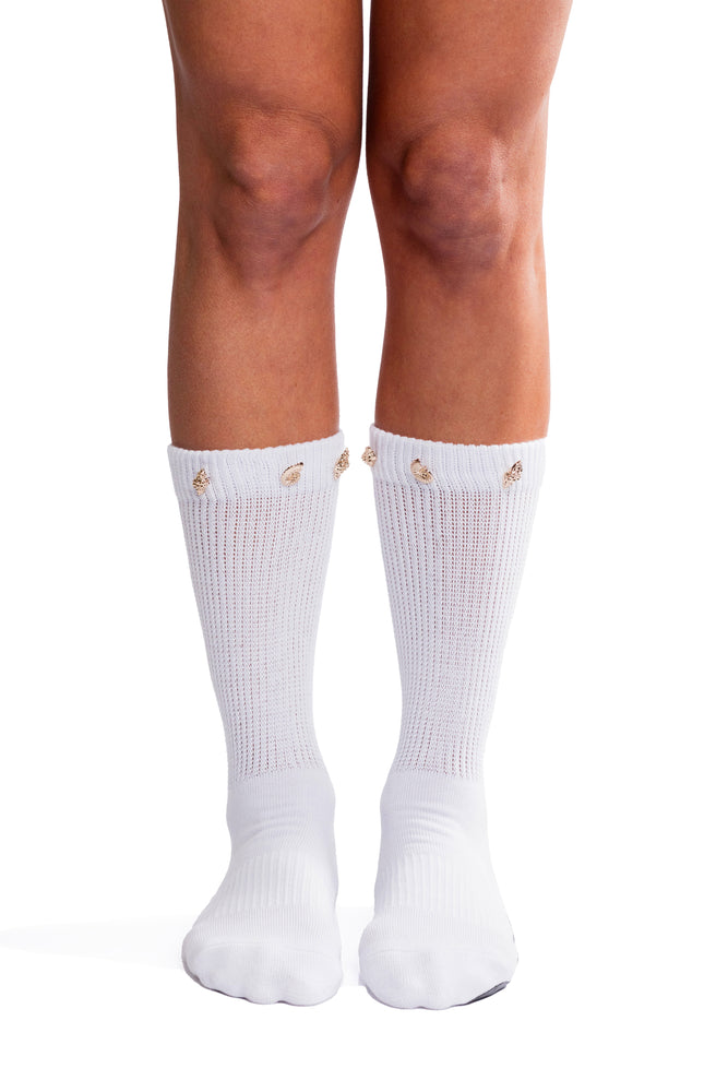 Detail shot of feet wearing white scrunch socks with gold seashell decoration on the cuff.