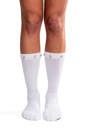 Detail shot of feet wearing white scrunch socks with gold seashell decoration on the cuff.