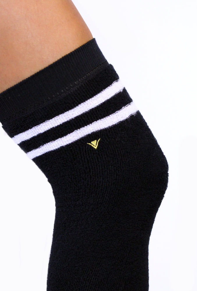 Detail picture of Arebesk gold logo embroidered on the side of black terry legwarmers with white stripes.