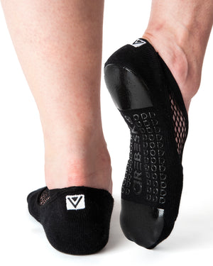 Back view of black ankle height, scooped grip socks with a diagonal mesh panel extending from the outside of the ankle to the top of the toes. Grip design has a silicon pad on the ball of the foot and the heel, as well as grip spelling out 'Arebesk" surrounded by rows of additional a's in the center of the foot.