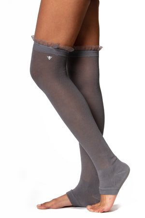 Side view of gray cotton over the knee legwarmer with a fitted heel and ruffle trim on the top seam.